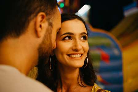 漂亮的黑发女孩看着右边和她的男友在晚上在西班牙的集市上闭着眼睛的胡子。关闭肖像