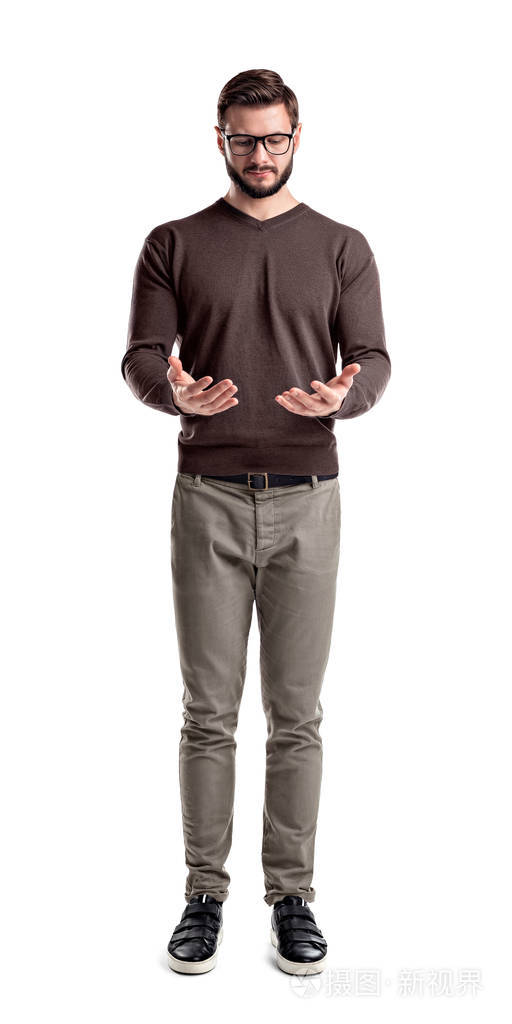 一个年轻的大胡子男子在货物裤看着他的双手, 仿佛拿着东西