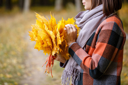 年轻时尚女性的肖像户外。在秋季公园的黑发妇女与时髦的格子大衣和围巾。手持黄色叶子