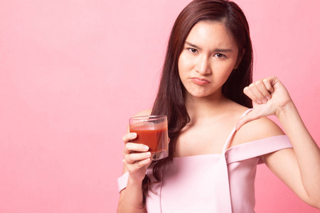 年轻的亚洲妇女讨厌番茄汁在粉红色的背景下