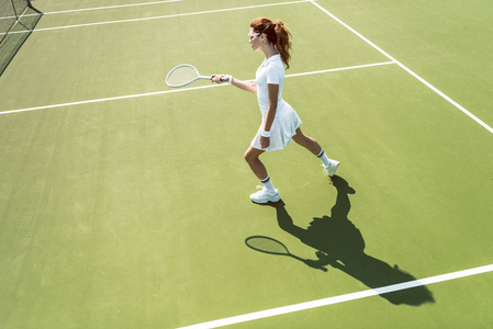 白色网球制服的年轻有魅力女子的侧面在球场上打网球照片