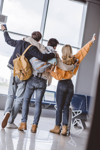 在机场与护照拥抱和举手的愉快的年轻朋友的背面视图