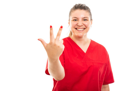 身穿红色擦洗的年轻医护护士肖像显示三号在白色背景上与 copyspace 广告区隔离的手势