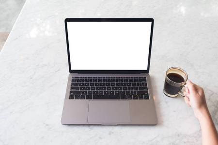 在咖啡馆的大理石桌上, 手持咖啡杯和笔记本电脑的一只手拿着一个空白白色桌面屏幕的图片