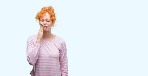 年轻的红发女人用手抚摸着嘴巴, 因为牙痛或牙齿疾病。牙医概念