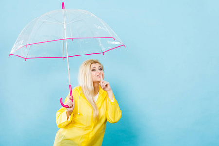 金发女人穿着黄色的雨衣，打着检查天气如果下雨显示沉默姿态的透明伞