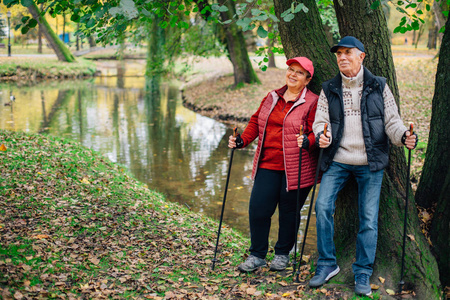美丽的一对夫妇站在五颜六色的秋季公园与北欧的步行杆。成熟的妇女和老人在户外休息