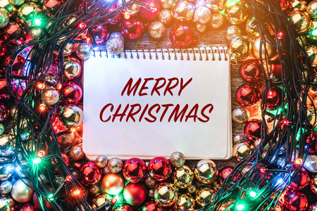 圣诞节的背景是红色和金色的小东西, 在笔记本周围点燃, 为圣诞快乐的信息。顶部视图。圣诞卡。光效