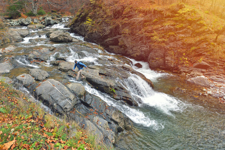 男性徒步者与背包走在岩石和瀑布在森林, 秋天的环境