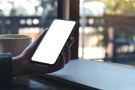 一个女人的手拿着黑色手机与咖啡杯和笔记本电脑在咖啡馆桌上的照片