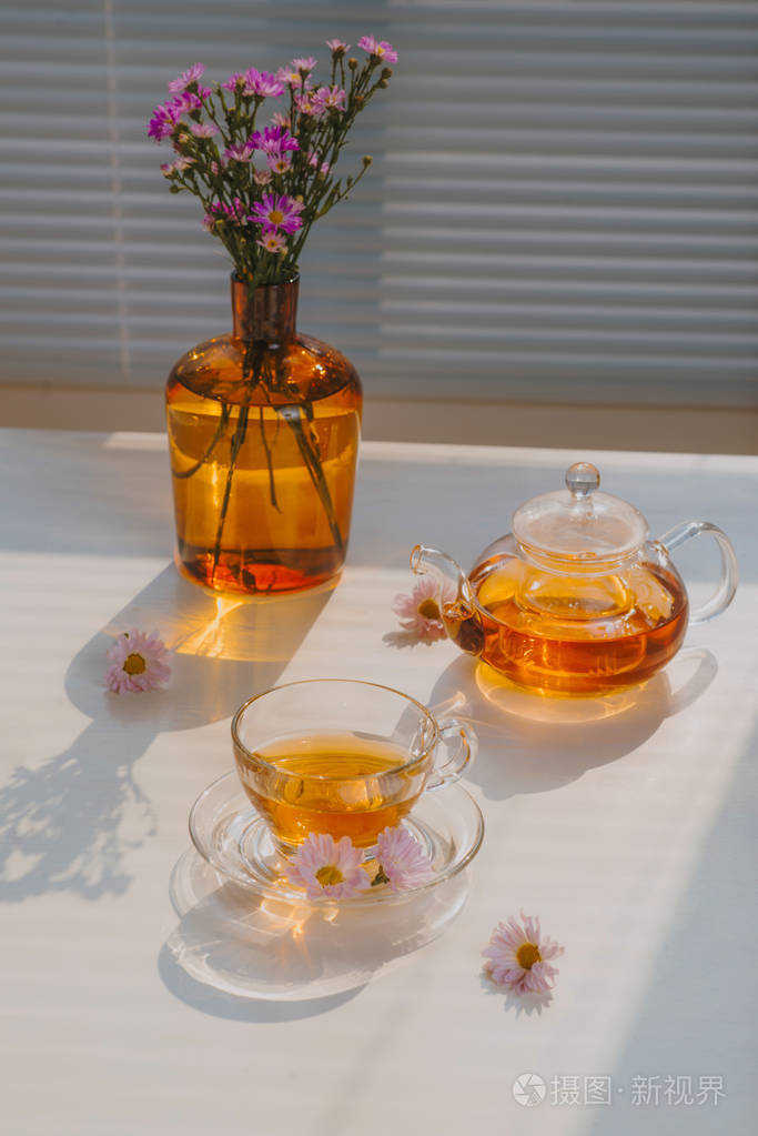 一杯茶在一个托盘和树枝上的桌子上的花朵在一个夏天晴朗的早晨的窗口