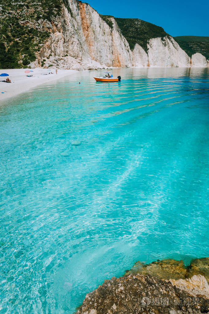 旅游游乐艇地到美丽的遥远的白卵石海滩与波纹透明的清澈湛蓝的海水.