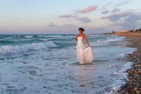 年轻的新娘在黄昏时享受寂寞走在沙滩上