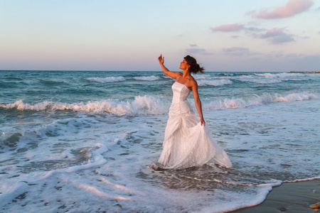 年轻的新娘在黄昏时享受寂寞走在沙滩上