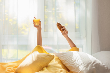 躺在毯子与羊角面包和玻璃橙汁在床上的昏昏欲睡妇女
