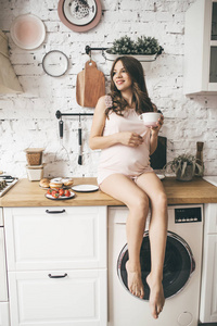 漂亮的孕妇在厨房里吃早餐和杯茶