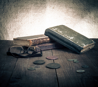 老式书籍和硬币和旧木桌上的眼镜。语气