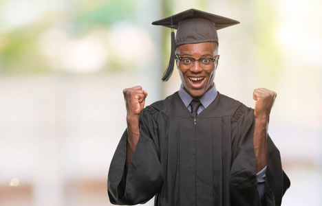 年轻毕业的非洲裔美国人在孤立的背景庆祝惊奇和惊奇为成功用胳膊升起和睁开眼睛。赢家理念