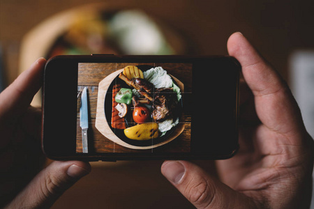 男士手拿手机拍照.关闭男性手手持现代智能手机, 在背景美味的晚餐.