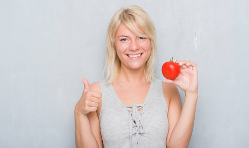 成年白种女人在灰墙上抱着新鲜的西红柿开心的笑着做 ok 标志, 拇指与手指, 优秀的标志