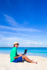 在地处热带的海滩在笔记本电脑上工作的年轻人
