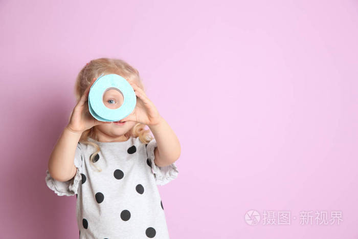 可爱的小女孩通过卫生纸卷上的颜色背景。文本的空间