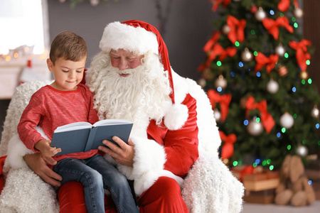 小男孩坐在正宗的圣诞老人的大腿上看书, 在室内