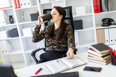一个年轻女孩坐在办公室里的电脑桌旁, 拿着一杯咖啡