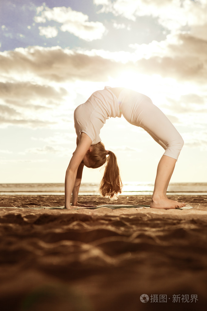 年轻漂亮苗条的女人练瑜伽母在沙滩上