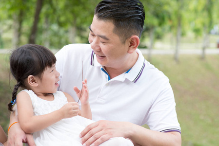 快乐的父亲和女儿在绿色公园的结合。亚洲家庭户外活动