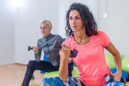 运动苗条的女人参加健身房健身类行使坐在 physioballs 做交替二头肌卷曲的哑铃