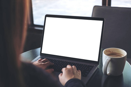 商业妇女的样机图像在笔记本电脑上使用和打字空白的白色屏幕和咖啡杯桌上的咖啡馆