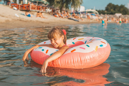 炎热的夏天, 快乐的小女孩带着充气戒指在水中游泳。孩子们学习游泳。儿童水玩具