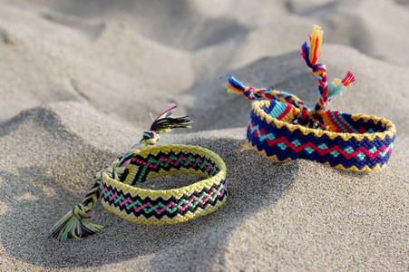 友谊的天然手镯, 五颜六色的编织友谊手镯, 背景, 彩虹色, 方格图案, 在沙滩上的沙子