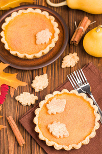 南瓜馅饼与肉桂和饼干在棕色餐巾木背景与秋季黄叶顶部视图近距离摄影季节性美国传统甜烘焙食品