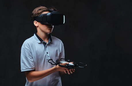穿着白色 t恤衫的年轻男孩使用虚拟现实玻璃, 并持有 quadcopter。在黑暗背景下被隔离