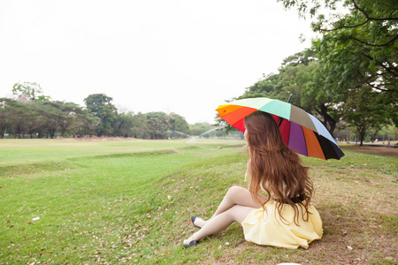 带着雨伞坐在草坪上的女人。