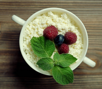 在一个碗中的树莓和蓝莓与成熟的浆果在质朴的木质背景的健康早餐平房干酪