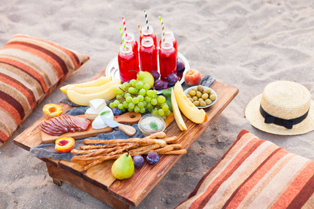 在日落的海滩上, 波西米亚的风格野餐。概念户外晚上健康膳食与果子和果汁