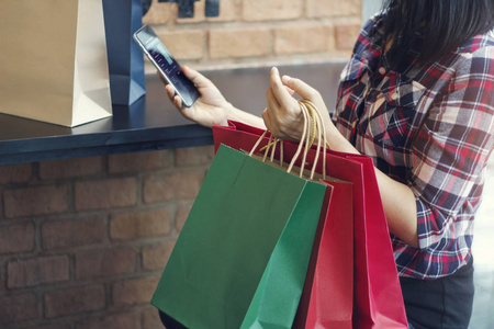 有购物袋的女人。在户外购物商场使用移动智能手机进行网上理财。所有在移动屏幕被设计了