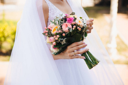 一个在美丽的白色婚礼刺绣礼服和面纱漫步在街上的一个裁剪新娘的特写, 握在她的手一束鲜艳的颜色新娘花束