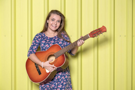 美丽的少女与声学吉他隔离在黄色的金属墙上