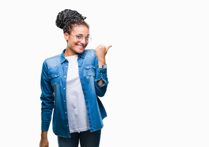 年轻的编织头发非洲裔美国女孩戴眼镜在孤立的背景微笑着与快乐的脸看, 用拇指指着一边