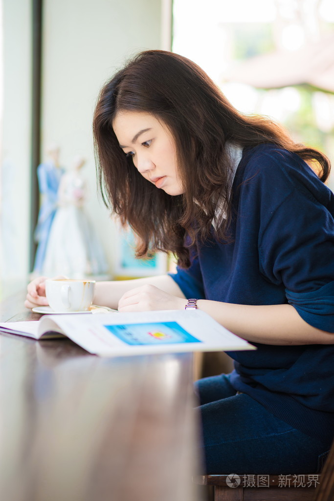 亚洲学生女人放松与热咖啡和杂志在咖啡馆