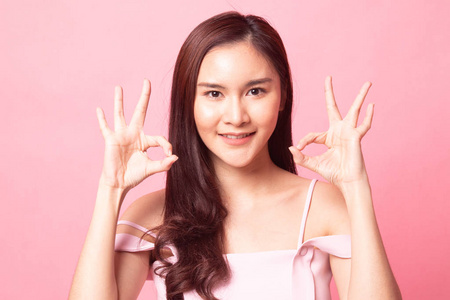 亚洲妇女显示双 Ok 手牌和粉红色背景的微笑