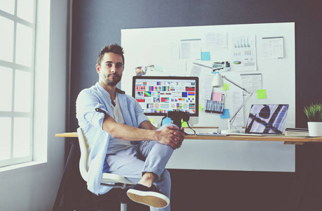 年轻设计师的肖像坐在平面工作室前的笔记本电脑和电脑, 而在线工作