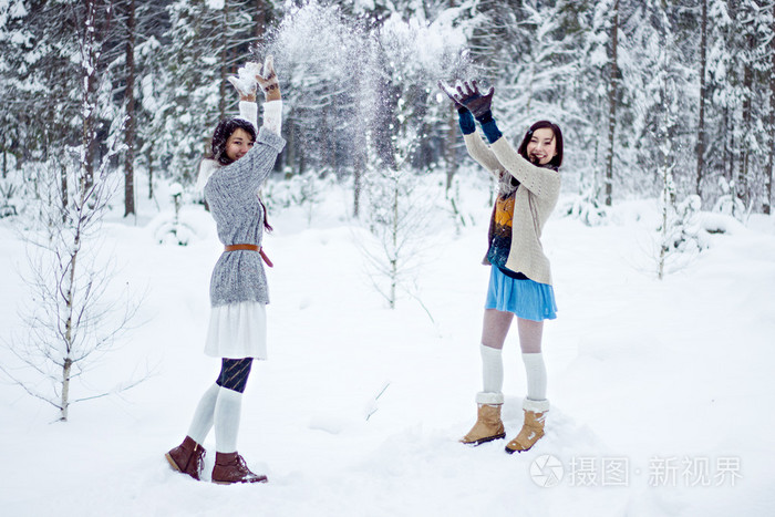时尚女性在暖和的毛衣，白色的森林背景上玩雪