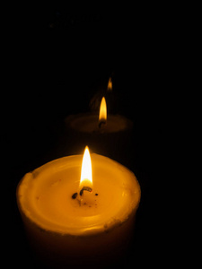 蜡烛在夜里燃烧。在黑暗中燃烧的白色蜡烛聚焦在一支蜡烛的前景