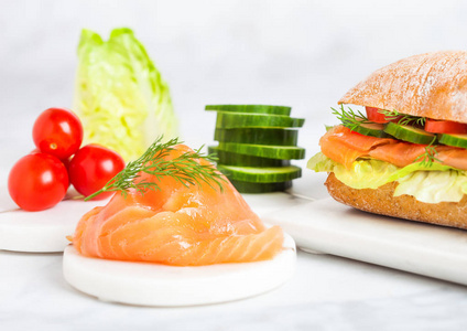 新鲜健康的鲑鱼三明治, 配生菜黄瓜和大理石板上的西红柿, 白色大理石背景。饮食健康食品
