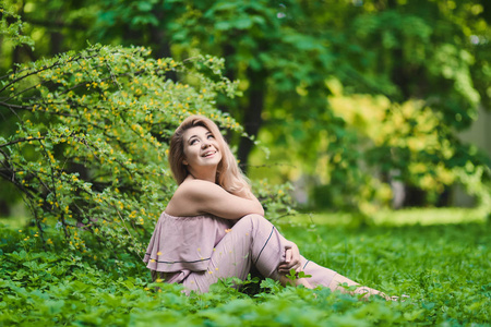 肖像美丽的年轻金发女孩与肿胀的嘴唇和的女性身体摆在绿色公园在阳光明媚的一天